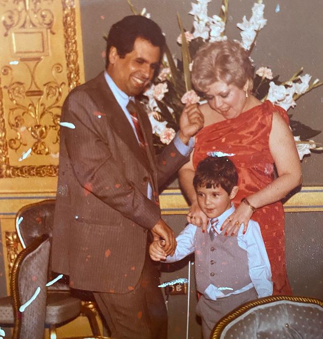 Childhood photo of J.R. Ramirez in a light blue shirt and grey half coat with his father in brown suit and his mother in a red gown.